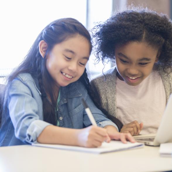 Two smiling children write at table