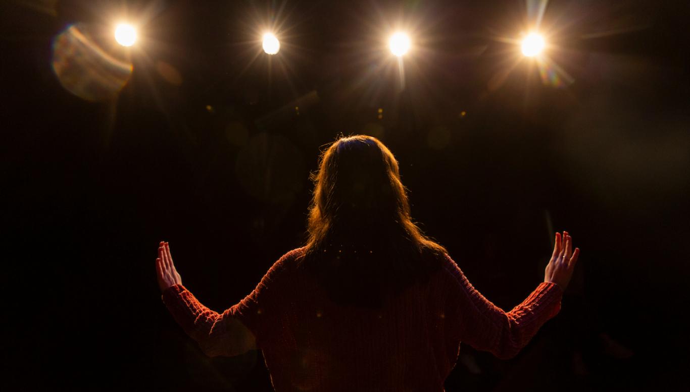 Student stands on stage in front of spotlights