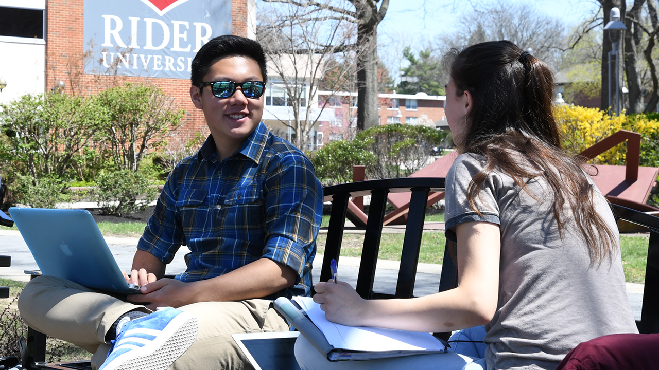 Two students sit on bench talking