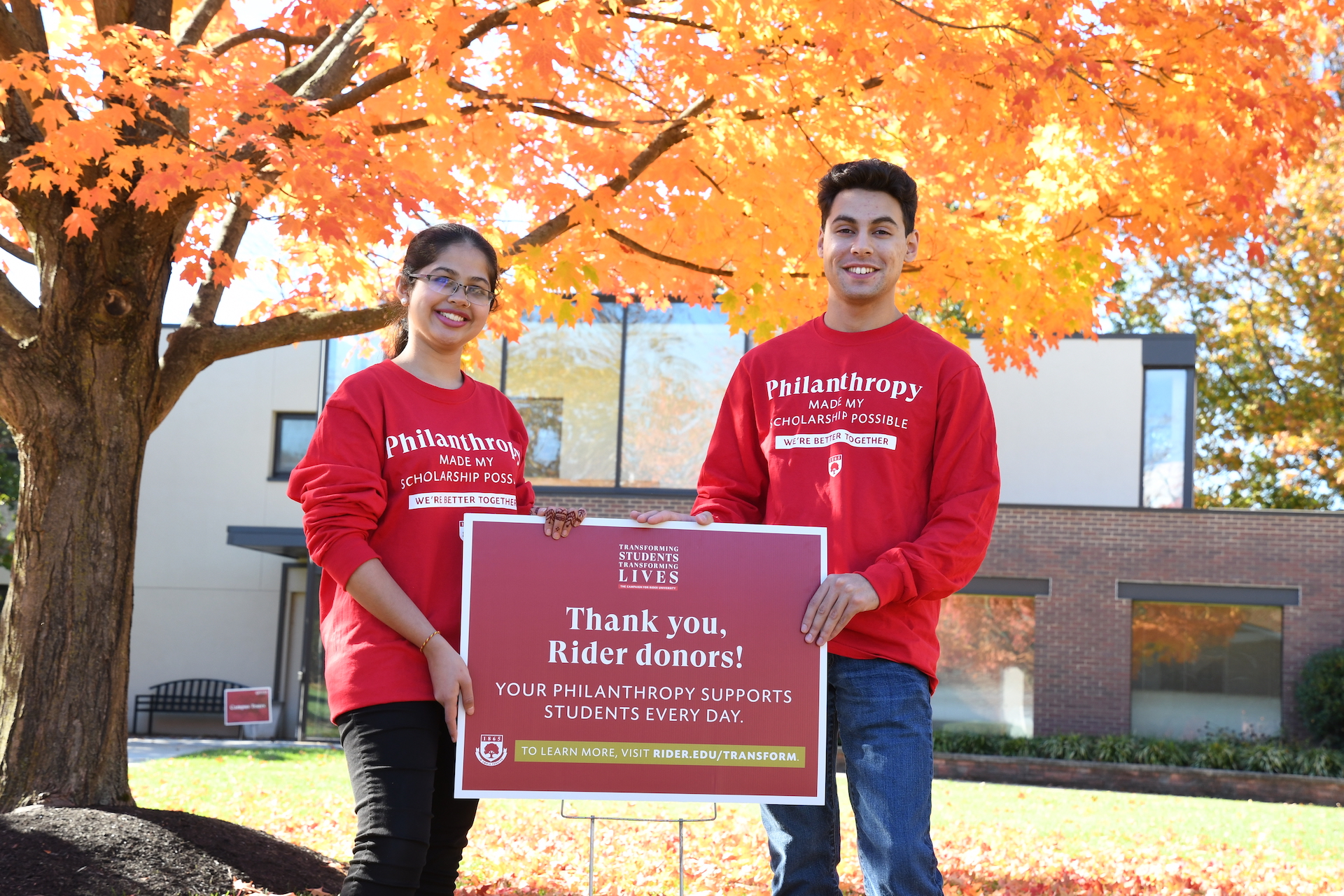 Two students stand outside holding a sign