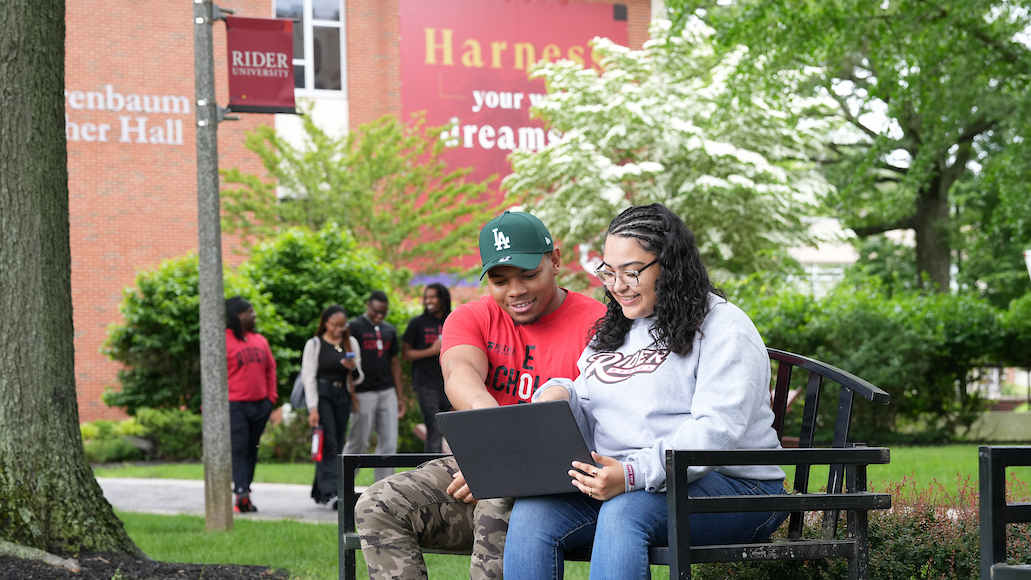 Students sitting on bench looking at laptop