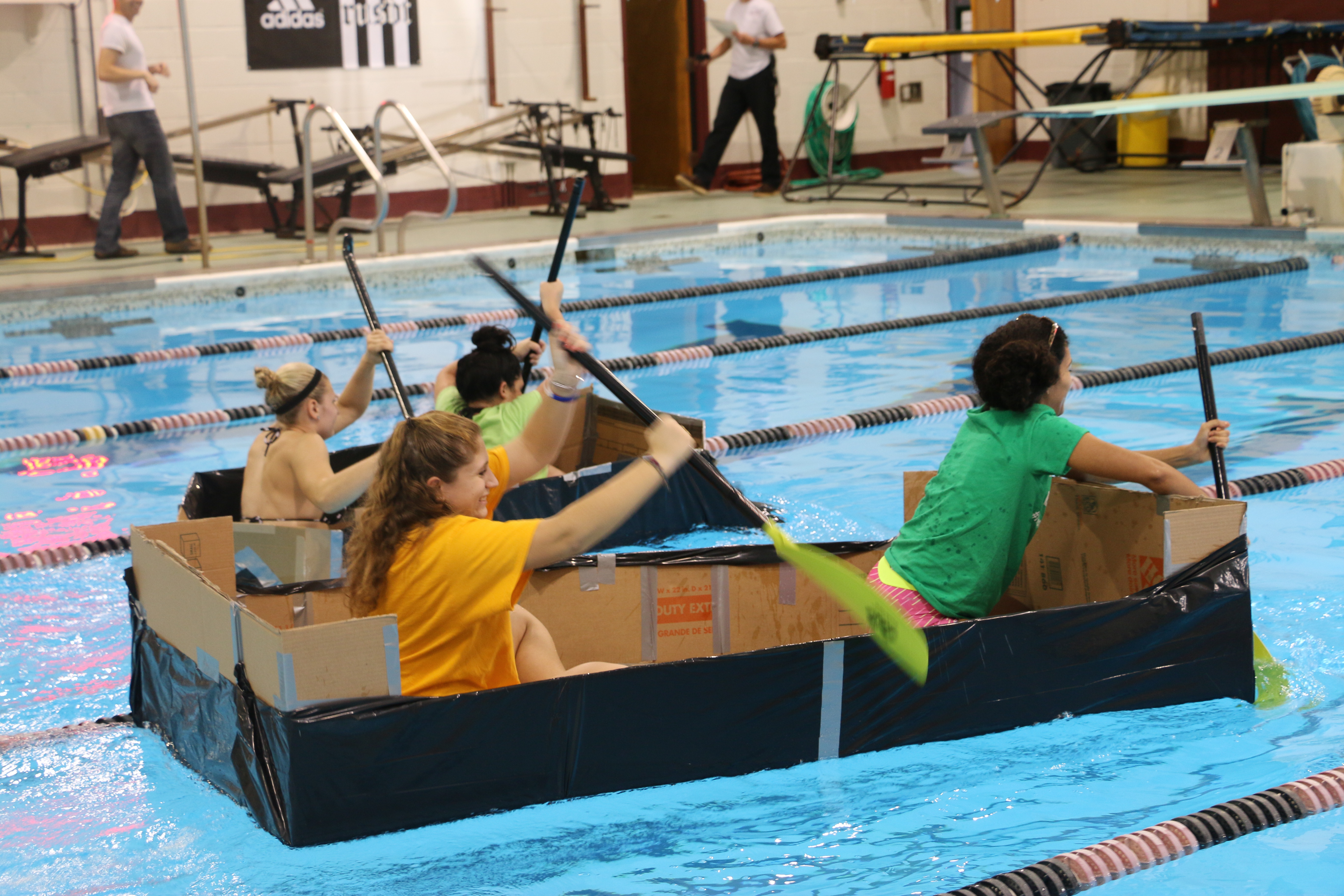 Students paddle in a cardboard boat across pool.