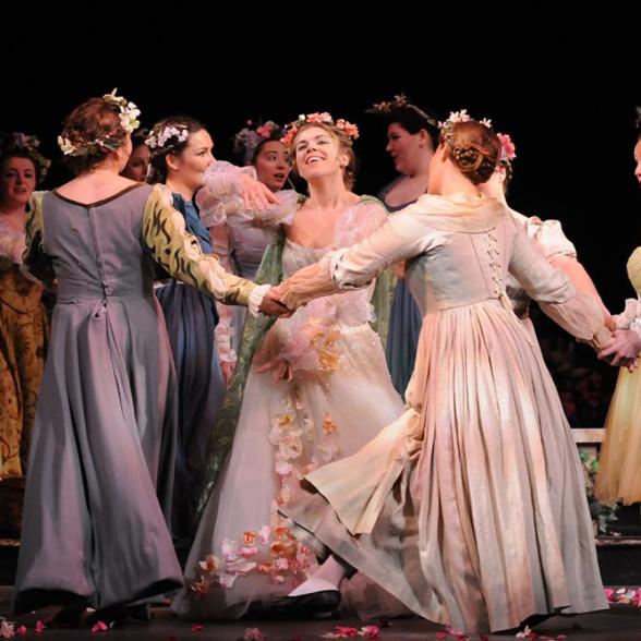 Female students on stage dressed in floral gowns dancing and singing together in an opera