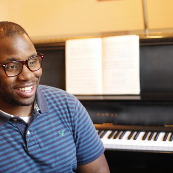 Male student smiles in front of a black piano
