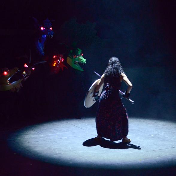 A female in the spot light faces off a dragon on stage