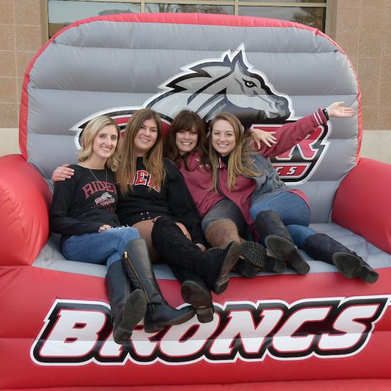 Four women sit on blow-up chair that says "Broncs"