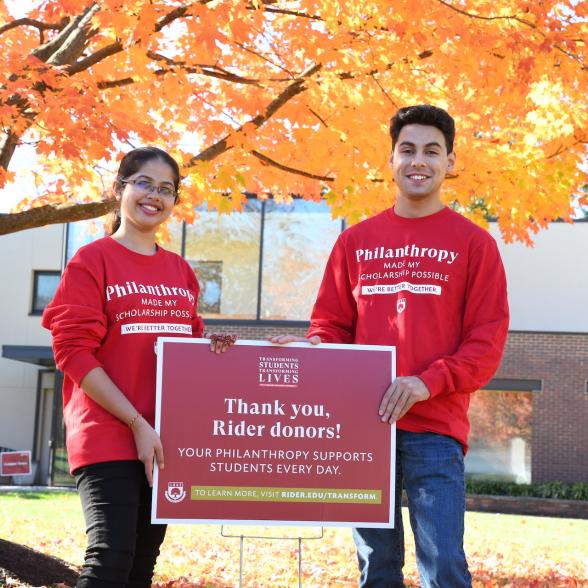 Two students stand outside holding a sign