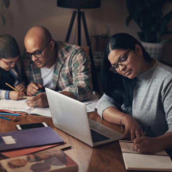 Man does homework with boy, woman works on laptop