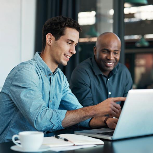 Two men sit at table and look at computer