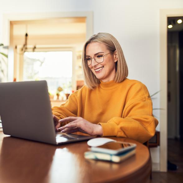 Woman sits at table smiling while looking at computer