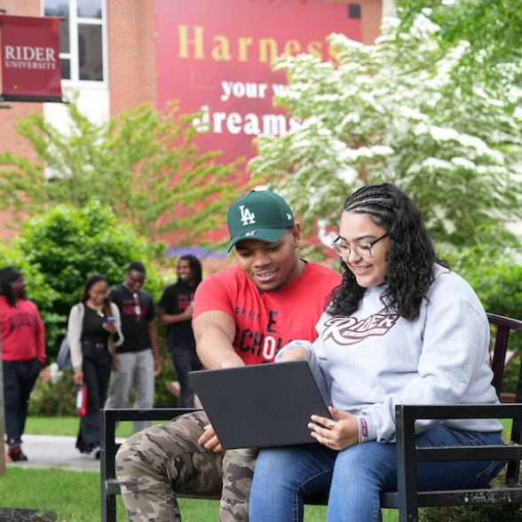 Students sitting on bench looking at laptop