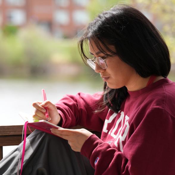 Rider student writing in notebook with lake in the background