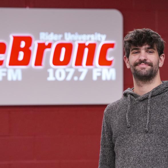 Owen McCarron stands in front of a sign for 107.7 The Bronc 