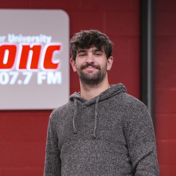 Owen McCarron stands in front of a sign for 107.7 The Bronc 