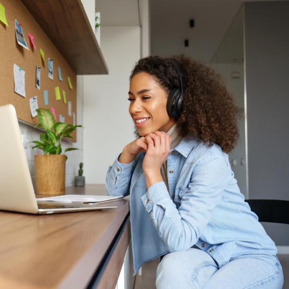 Smiling young woman wearing headphones and looking at computer