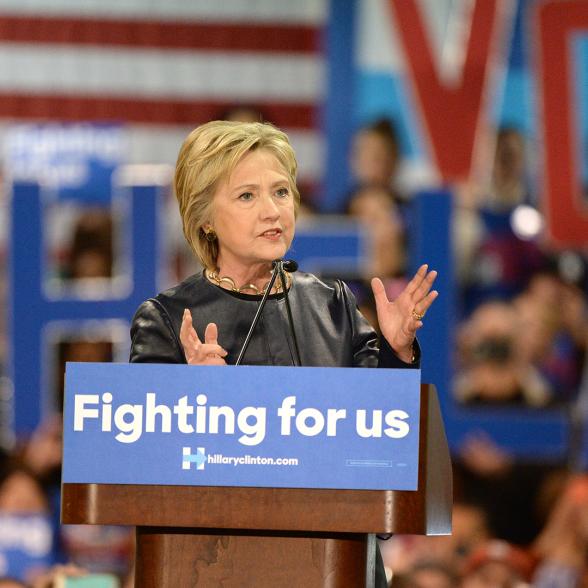 Hillary Clinton at a lectern with the words "Fighting for us