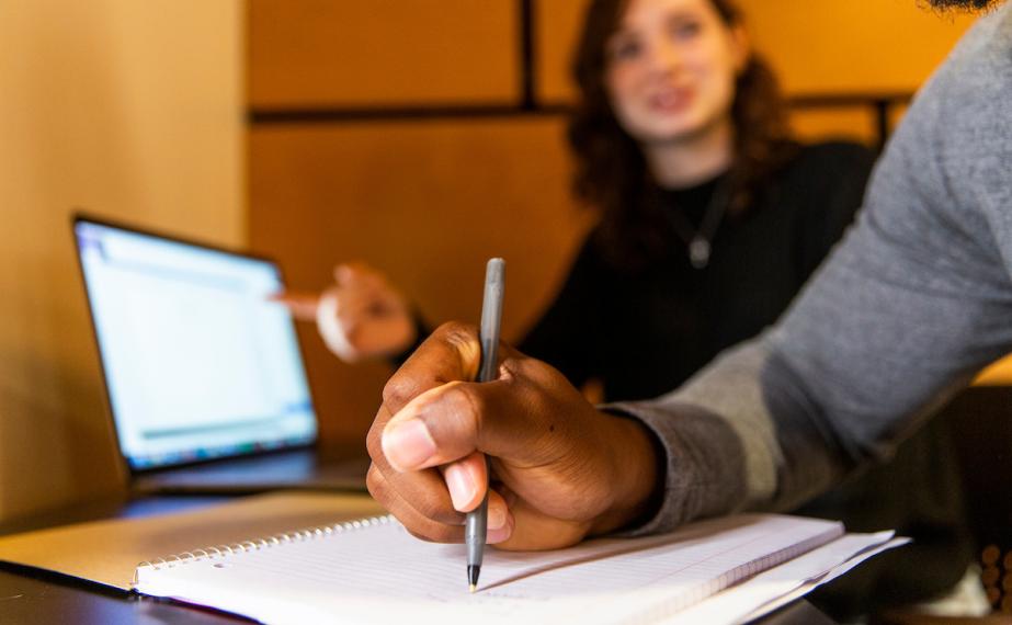 Student holds pen to notepad while working with a fellow student