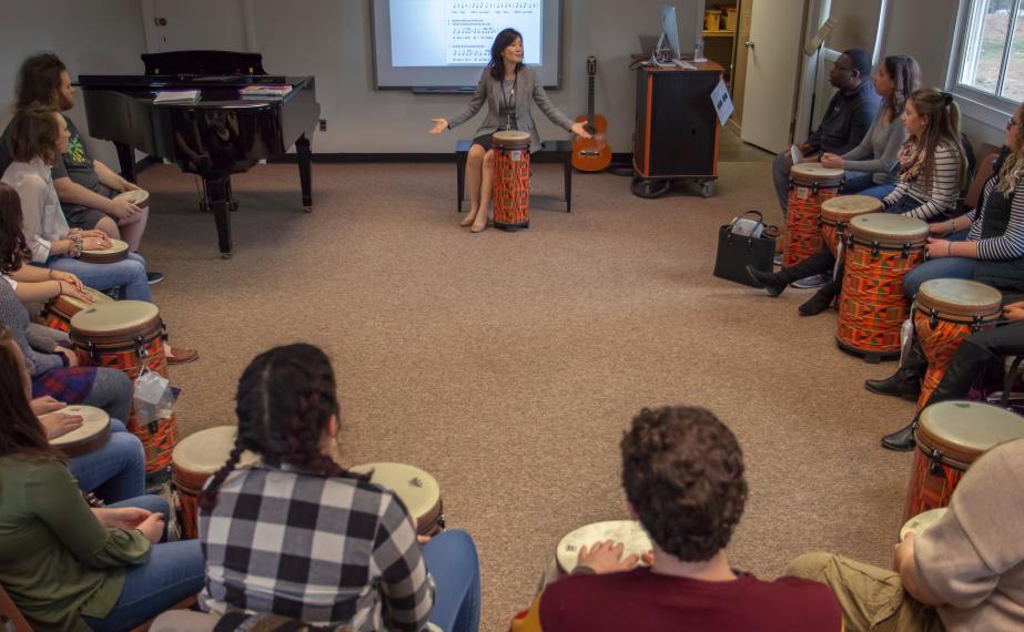 Music educator sits in a circle of students with bongos giving a lecture