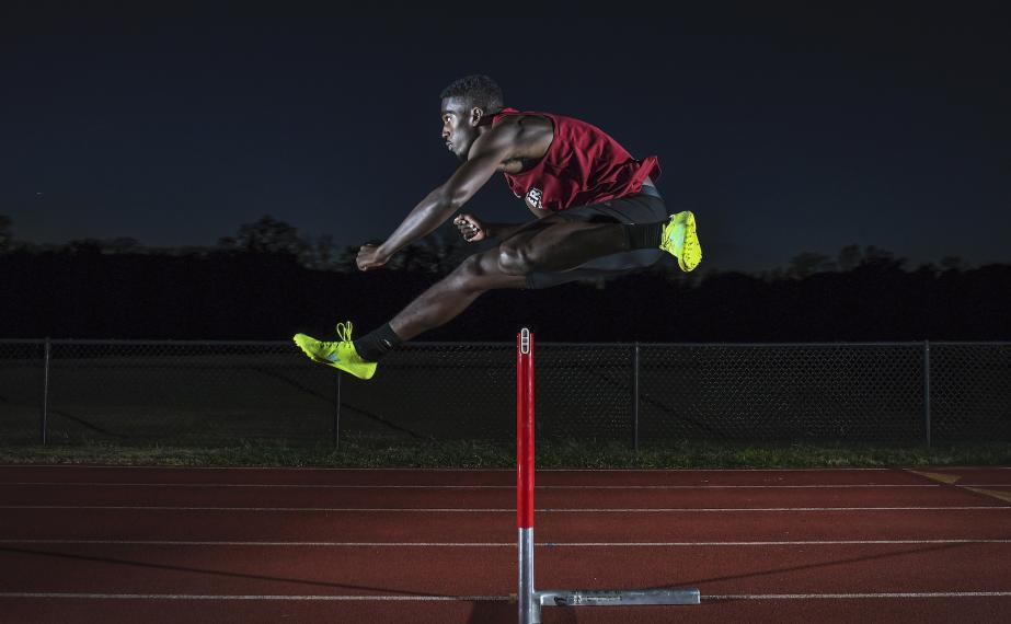 Division I athlete jumps hurdle on track