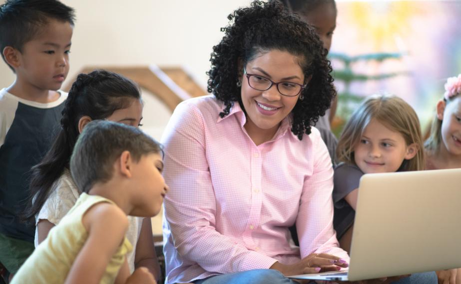 Teacher Sitting on the Floor With a Laptop and Students