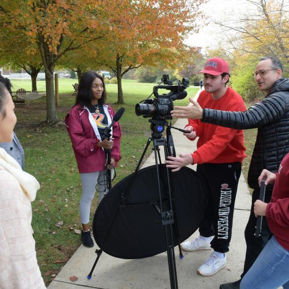 Students and a teacher around a film camera outside