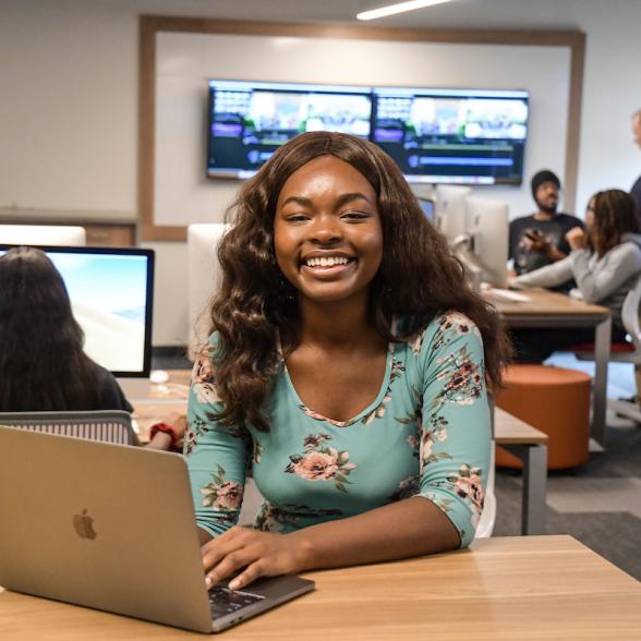 Female student smiles in media lab wit laptop