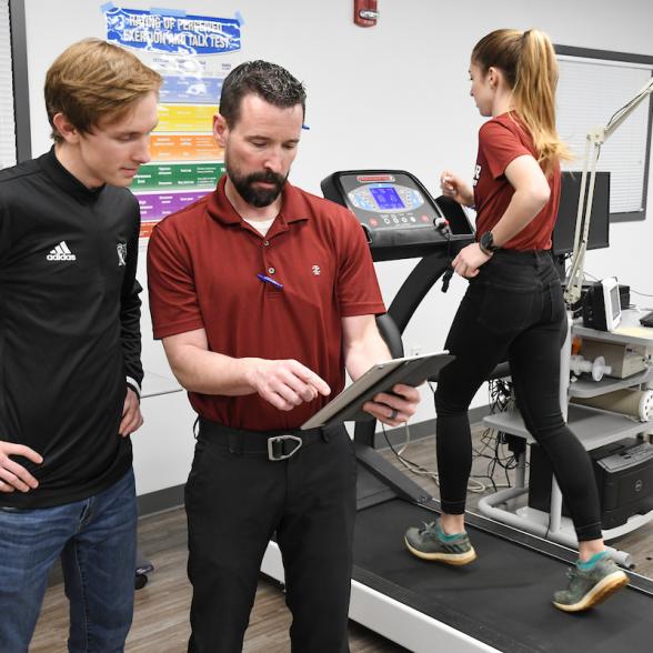 Faculty and students in the health lab going over reports from student on treadmill