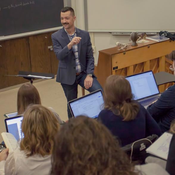 Faculty next to a piano teaches a classroom of students