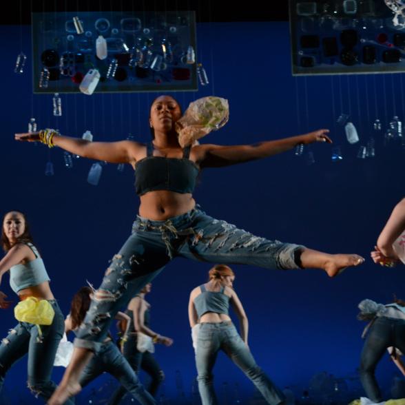 Female student mid air in dance pose on stage of recycled materials