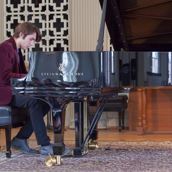 Male student in crimson blazer plays a masterful melody on a polished grand piano