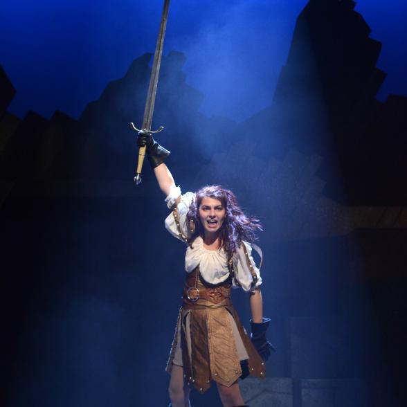 female stands at center stage and raises a sword