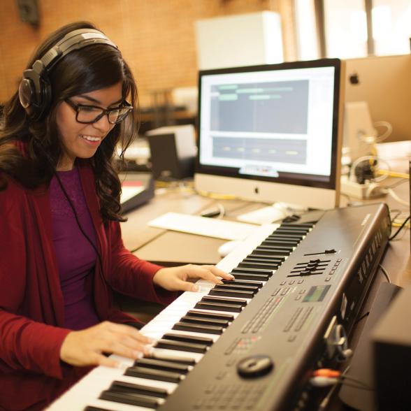 Female student sits at keyboard near her laptop, practicing.