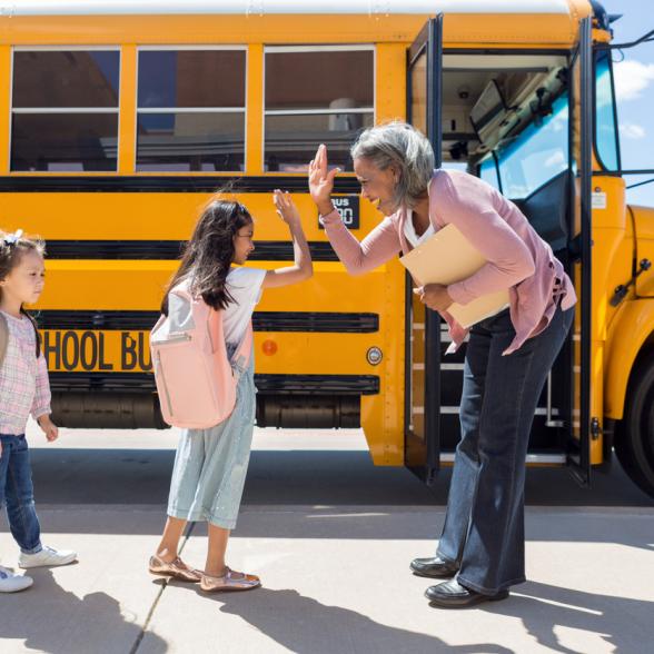 Woman high-fives student in front of school bus