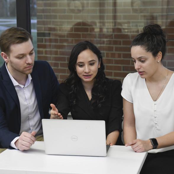 Three students look at laptop and have discussion