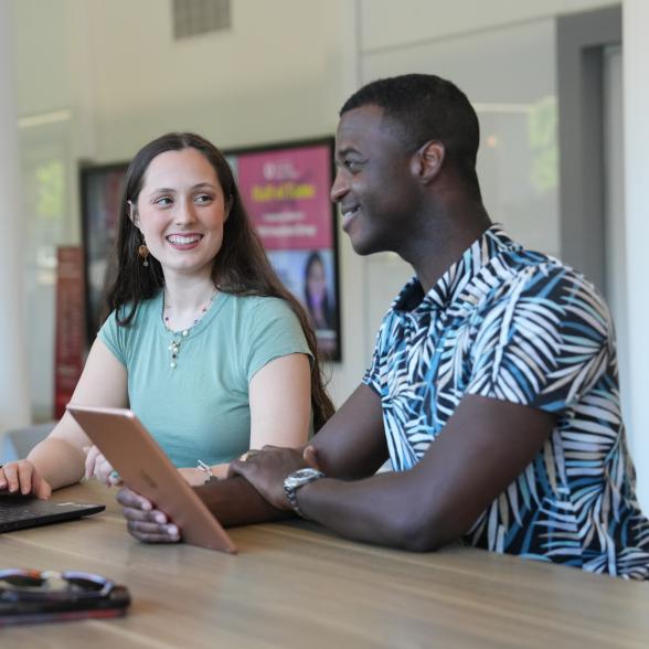Two graduate students on computers talking