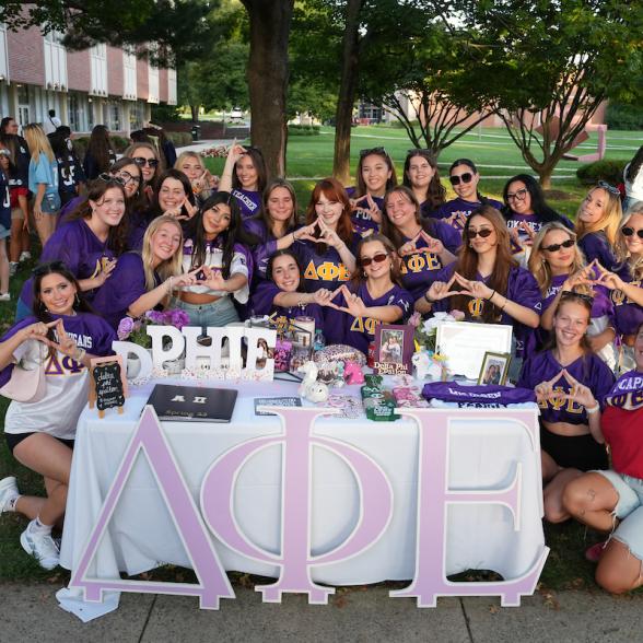 A group of sorority members pose together around a decorated table during an outdoor campus event at Rider University.