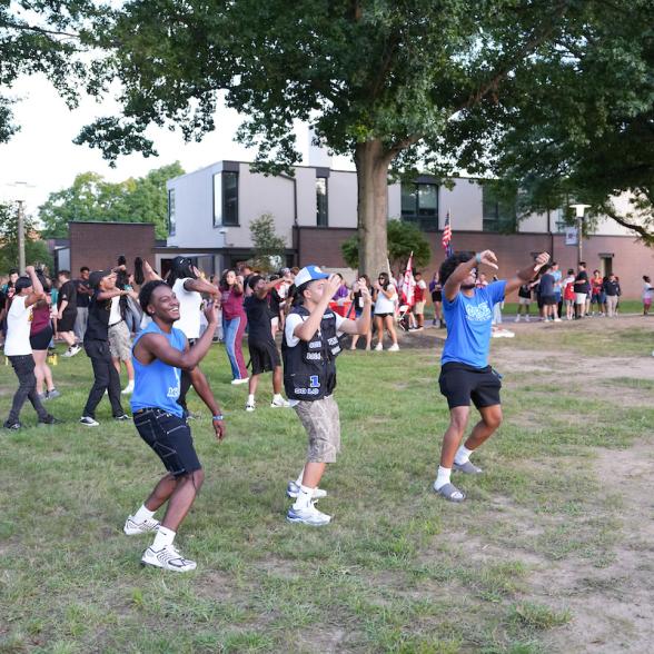 Students participate in an outdoor activity on Rider University's campus, with other students gathered on the lawn in the background.