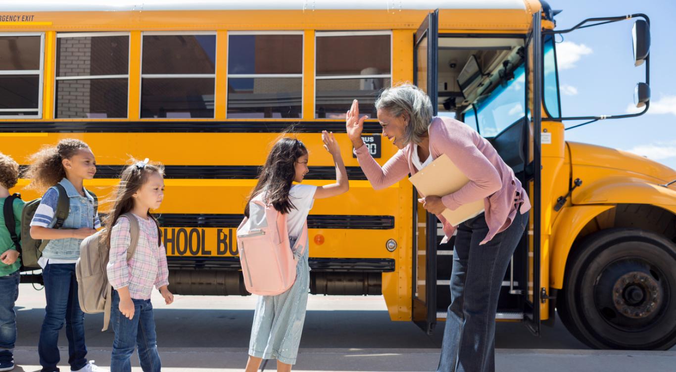 Woman high-fives student in front of school bus