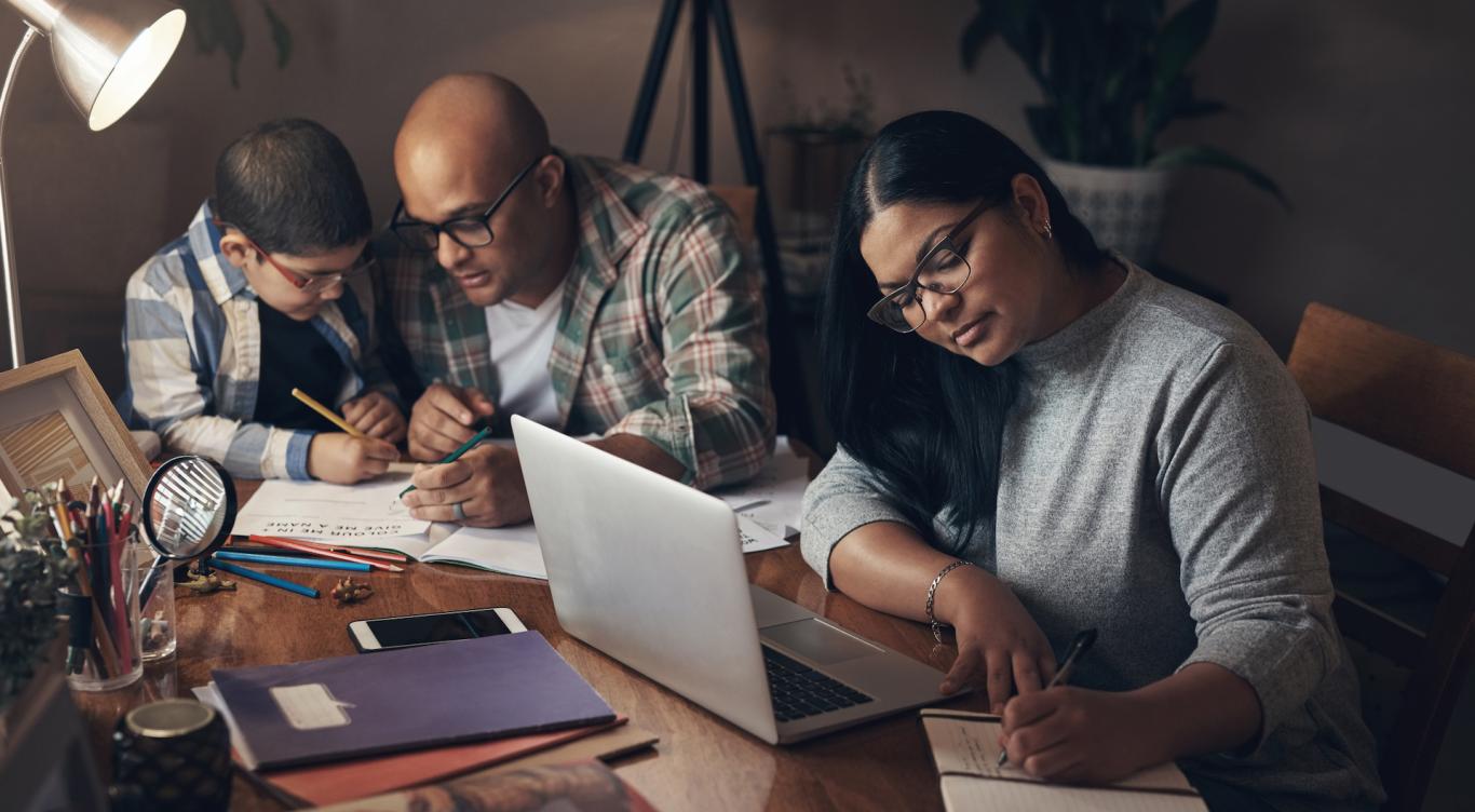 Man does homework with boy, woman works on laptop