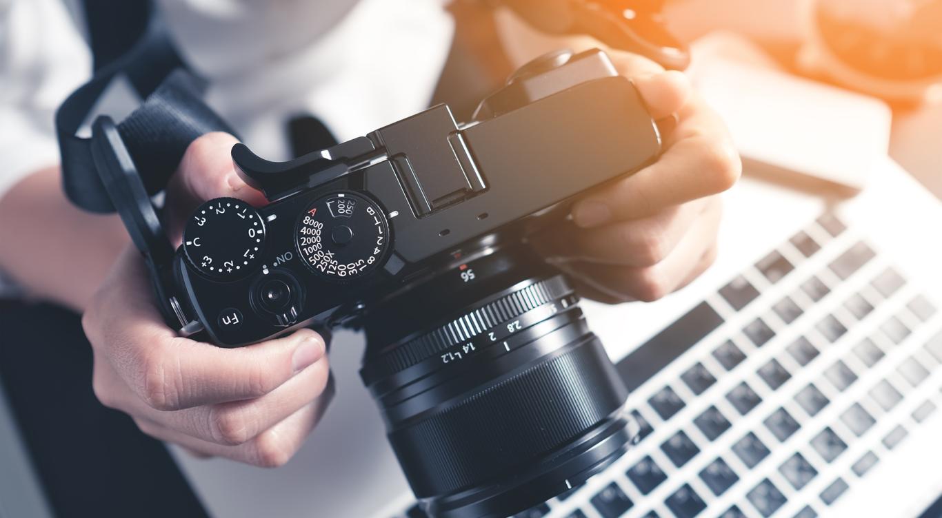 Photographer holding camera on desk ready to editing photos on laptop