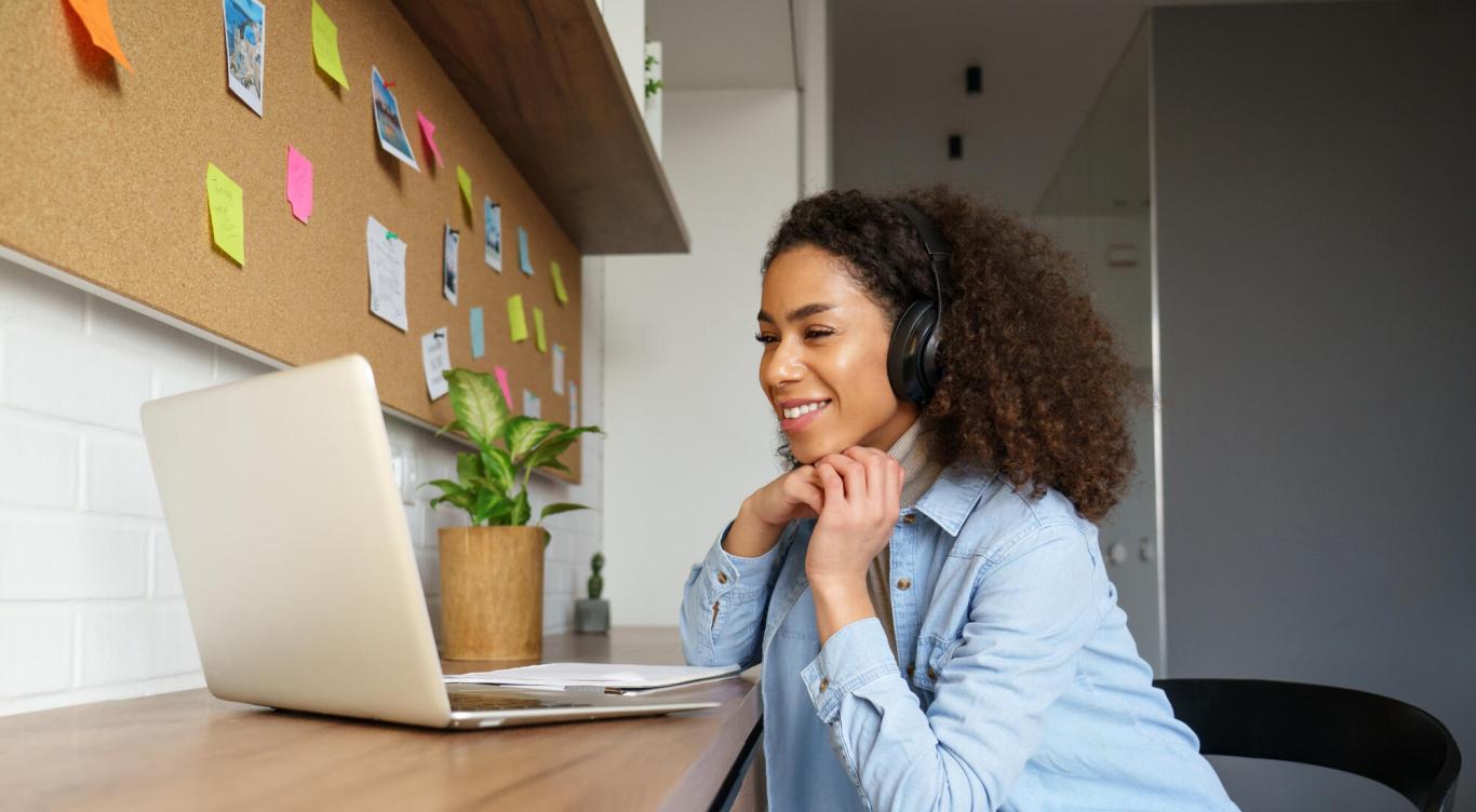 Smiling young woman wearing headphones and looking at computer