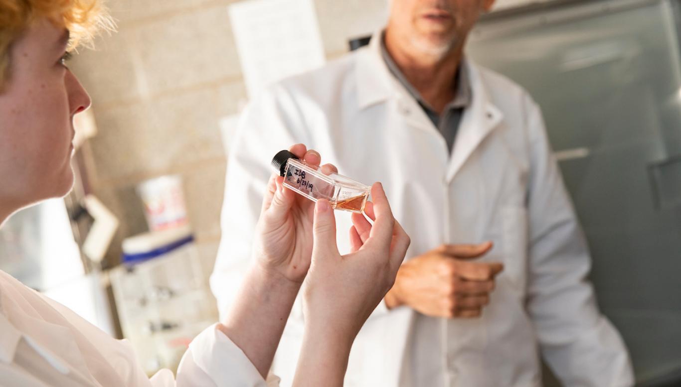 Student in lab coat working with teacher in biology classroom