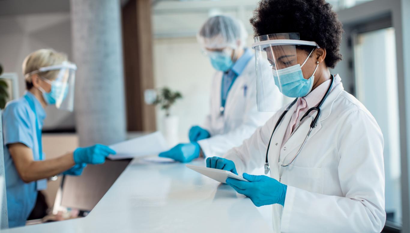 Woman with mask and face shield stands at reception desk 