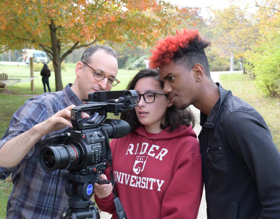 Two students and a professor looking through a large camera lens 