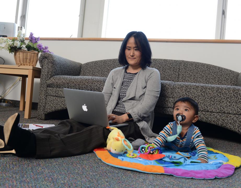 Woman works on laptop with baby next to her