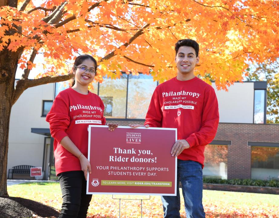 Two students stand outside holding a sign