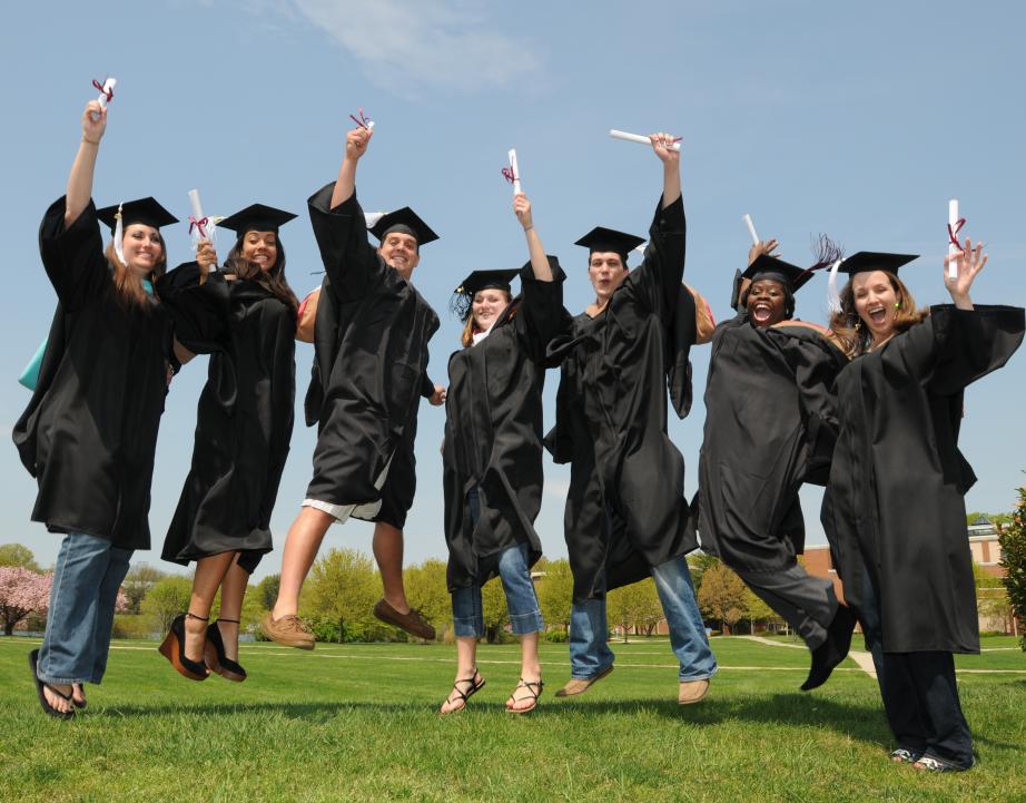 Rider students in graduate attire with diplomas celebrating and jumping on campus