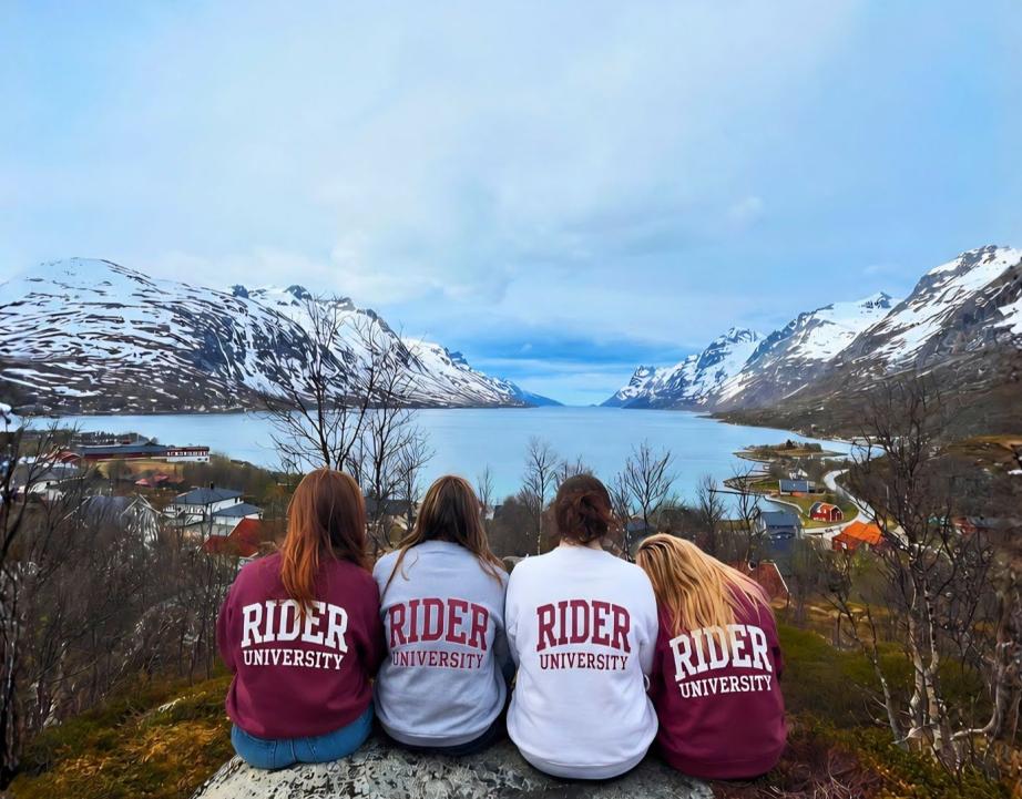 Students with Rider sweatshirts sitting and facing lake and mountains