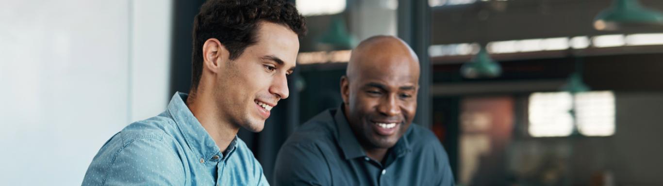 Two men sit at table and look at computer