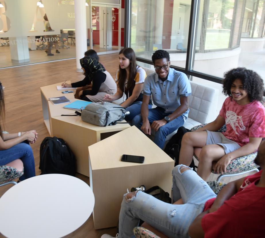 Students sit in lobby of business college talking.